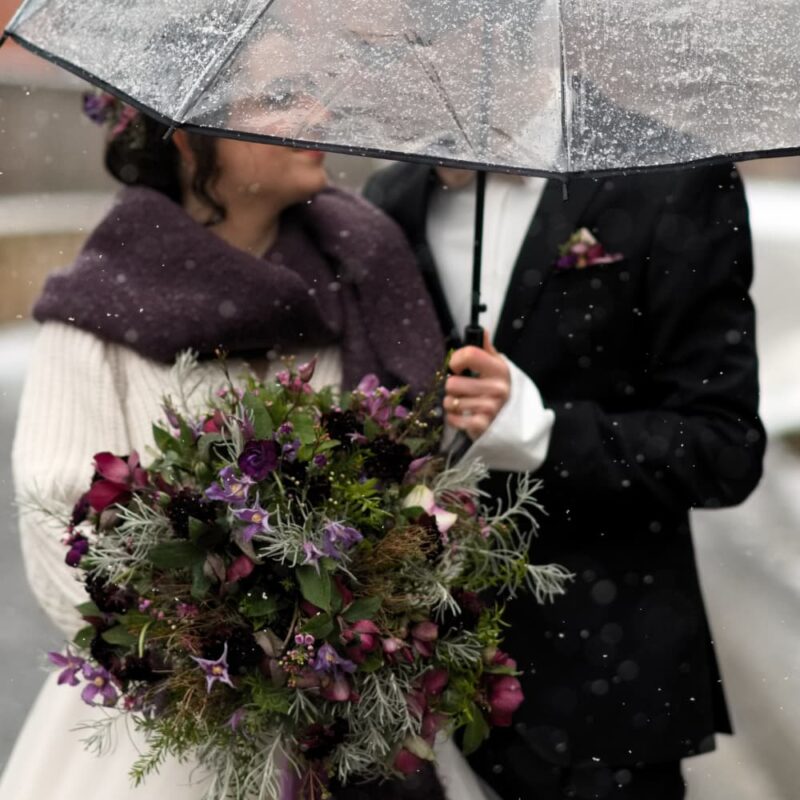Inga und Mirko mit winterlichem Brautstrauß unter einem Regenschirm im Schnee
