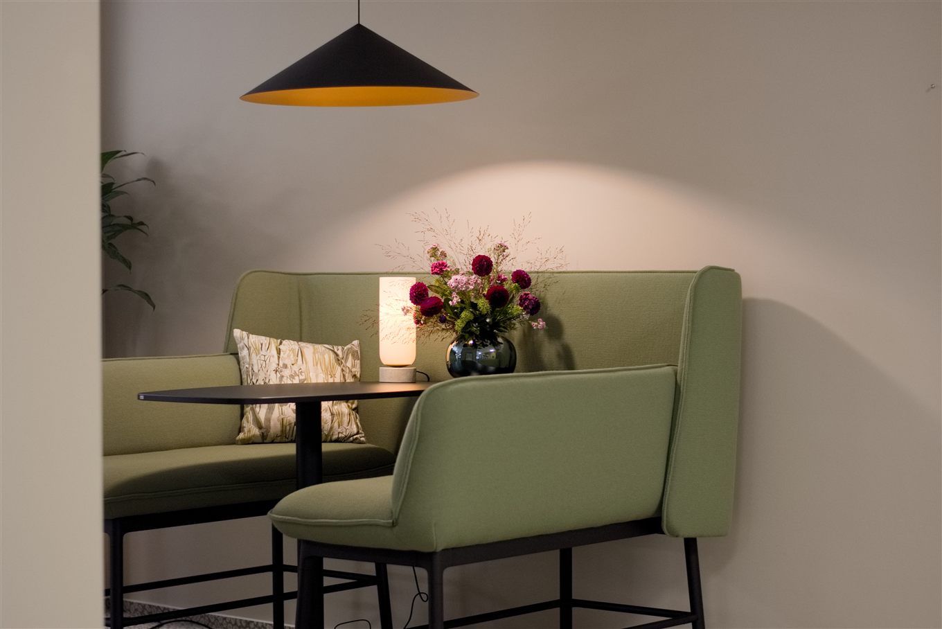 Geschützte Sitznische mit salbeigrünen Polstern, eigener Lichtquelle und floralem Arrangement.